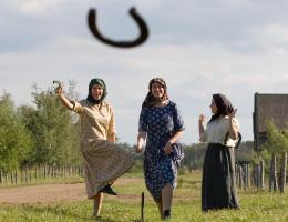 Three women in historical costume playing horseshoes